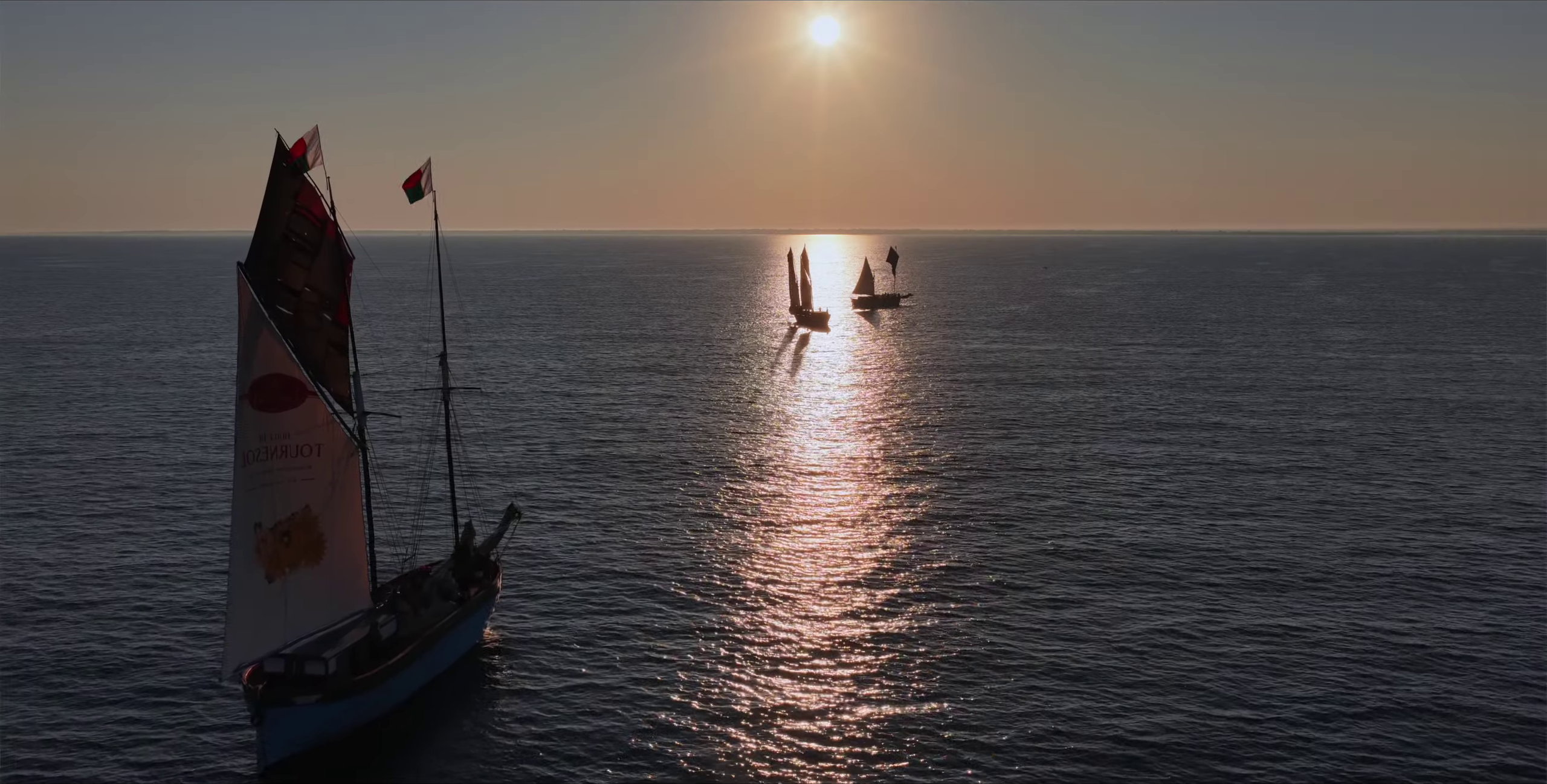 Boutres en silhouette au coucher du soleil doré avec drapeau malgache