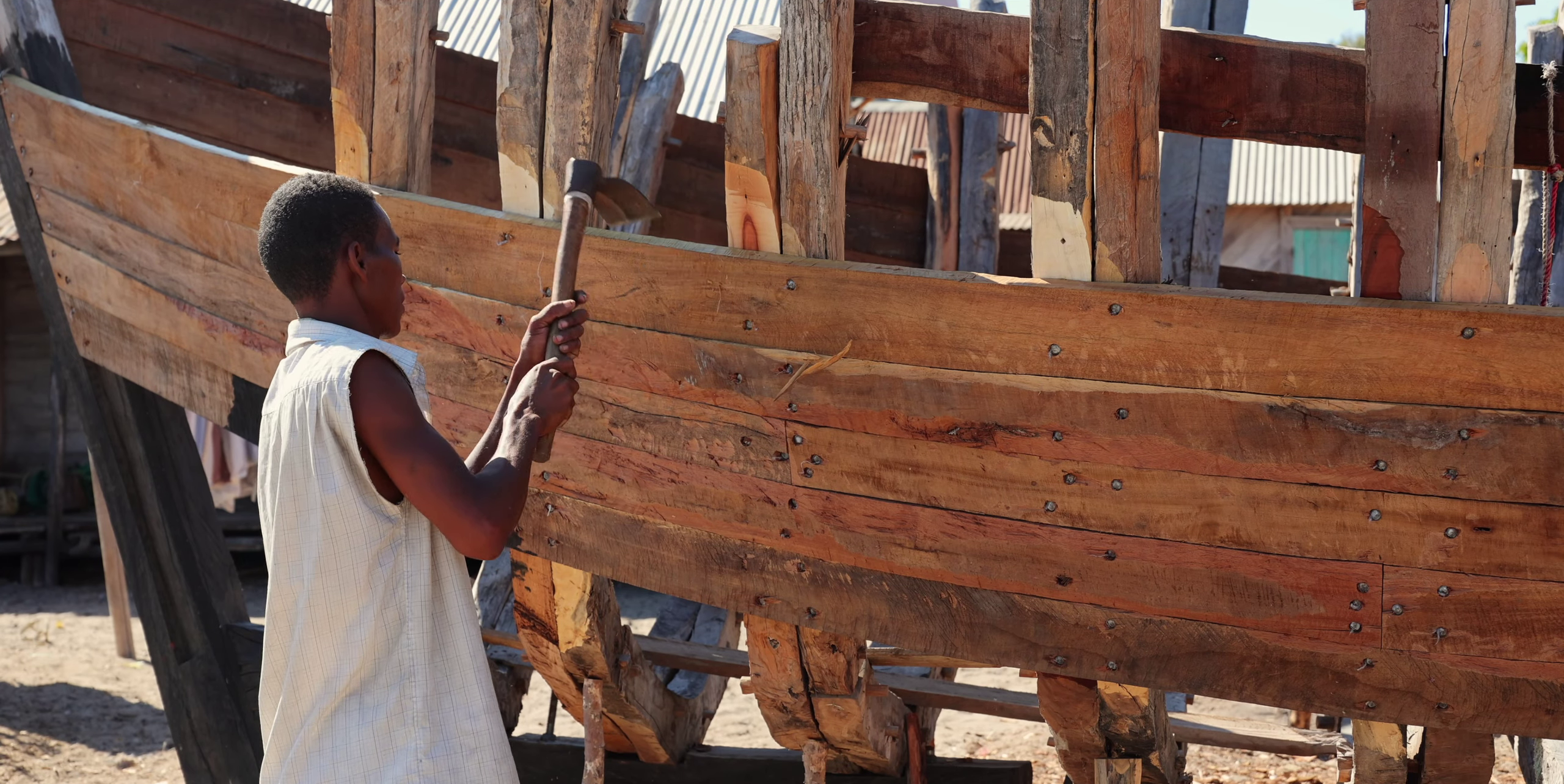 Jeune charpentier naval clouant les planches du bordé d'un boutre en construction