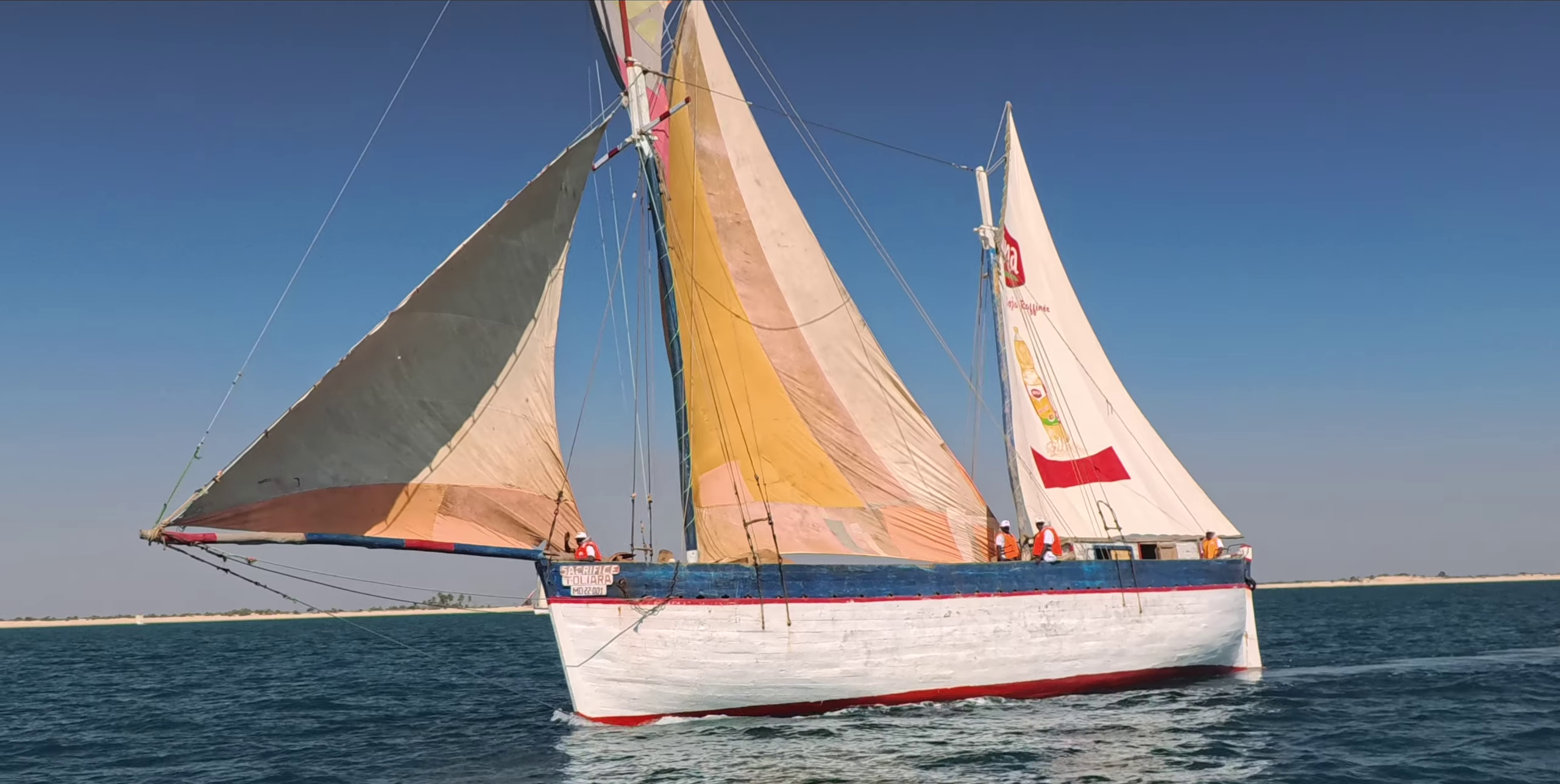 Goélette traditionnelle avec 3 voiles colorées naviguant en pleine mer bleue