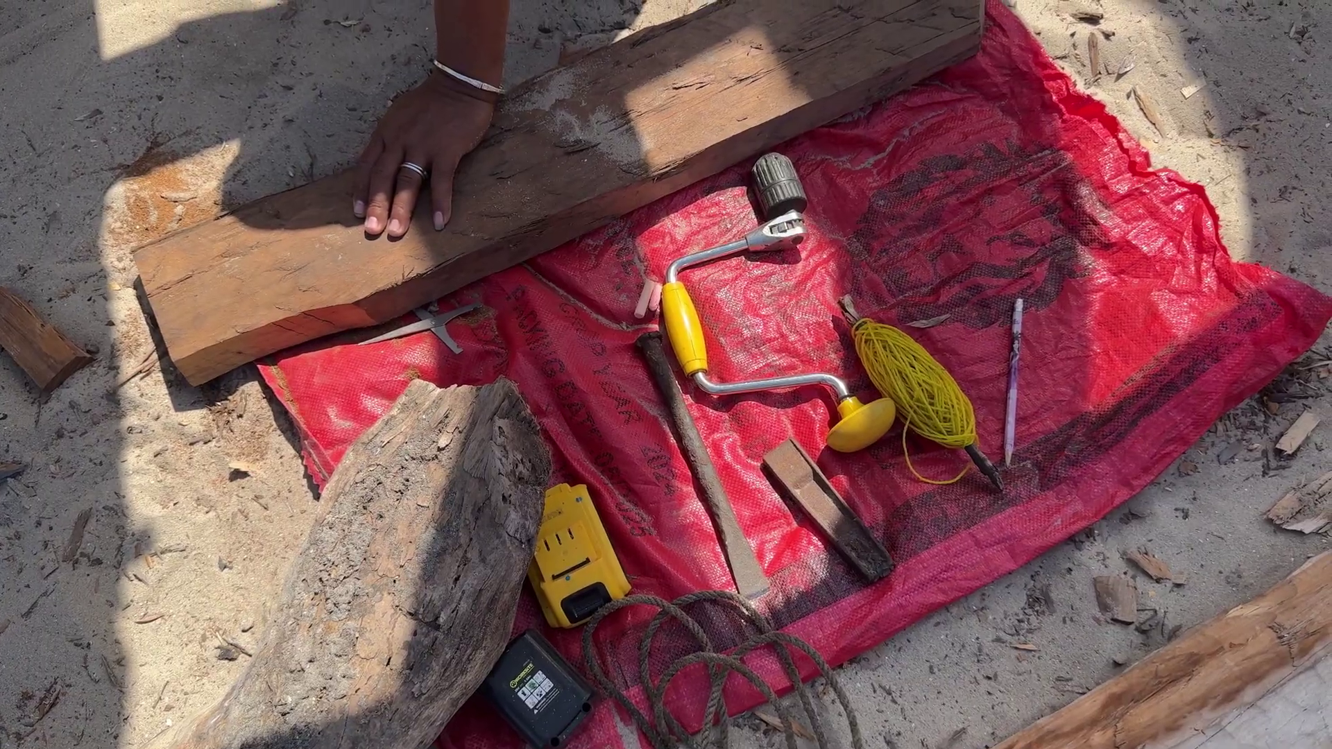 Outils de charpenterie navale traditionnels disposés sur une bâche rouge — vrille, masse, cordeau